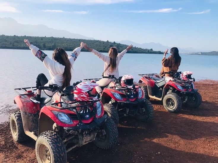 Trois copines assises sur des quads rouges au bord de l'eau, bras levés